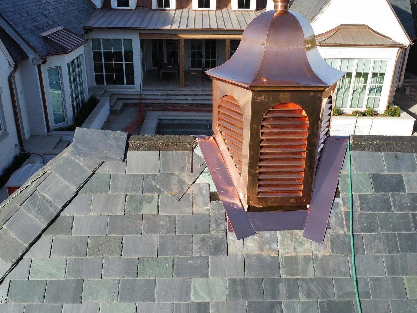 Copper cupola and standing-seam ridge on a finished slate roof, aerial detail