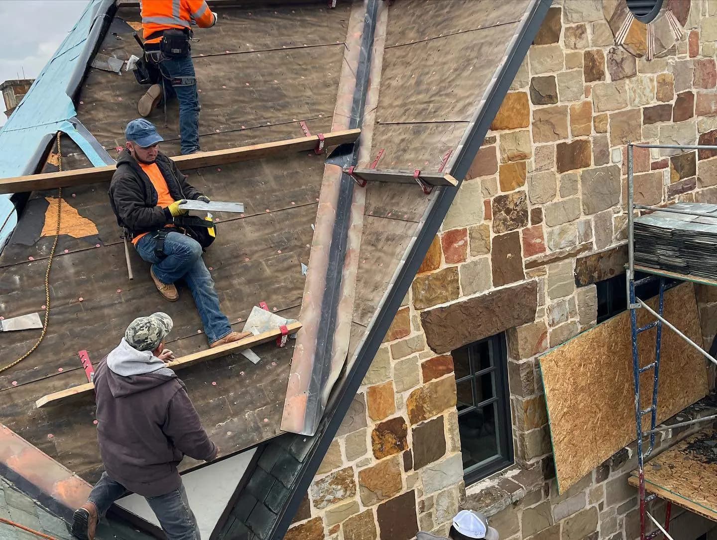 Slate roofing crew working around a new copper valley on a stone estate roof