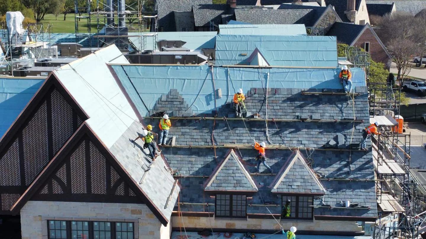 Aerial view of a large commercial slate roof installation with crews tied off