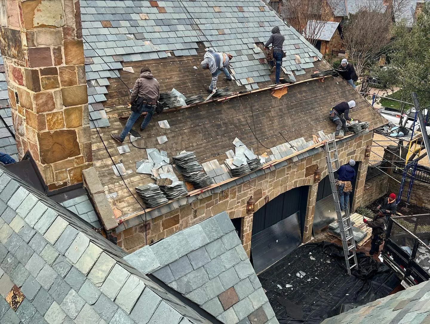 Specialty slate crew installing hand-cut slate on a steep stone mansion roof