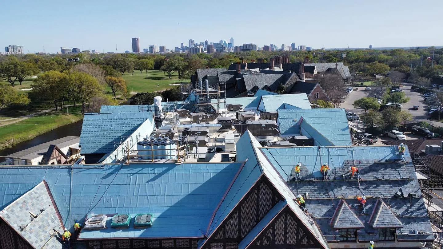 Aerial view of slate roofing crews working across a large steep roof