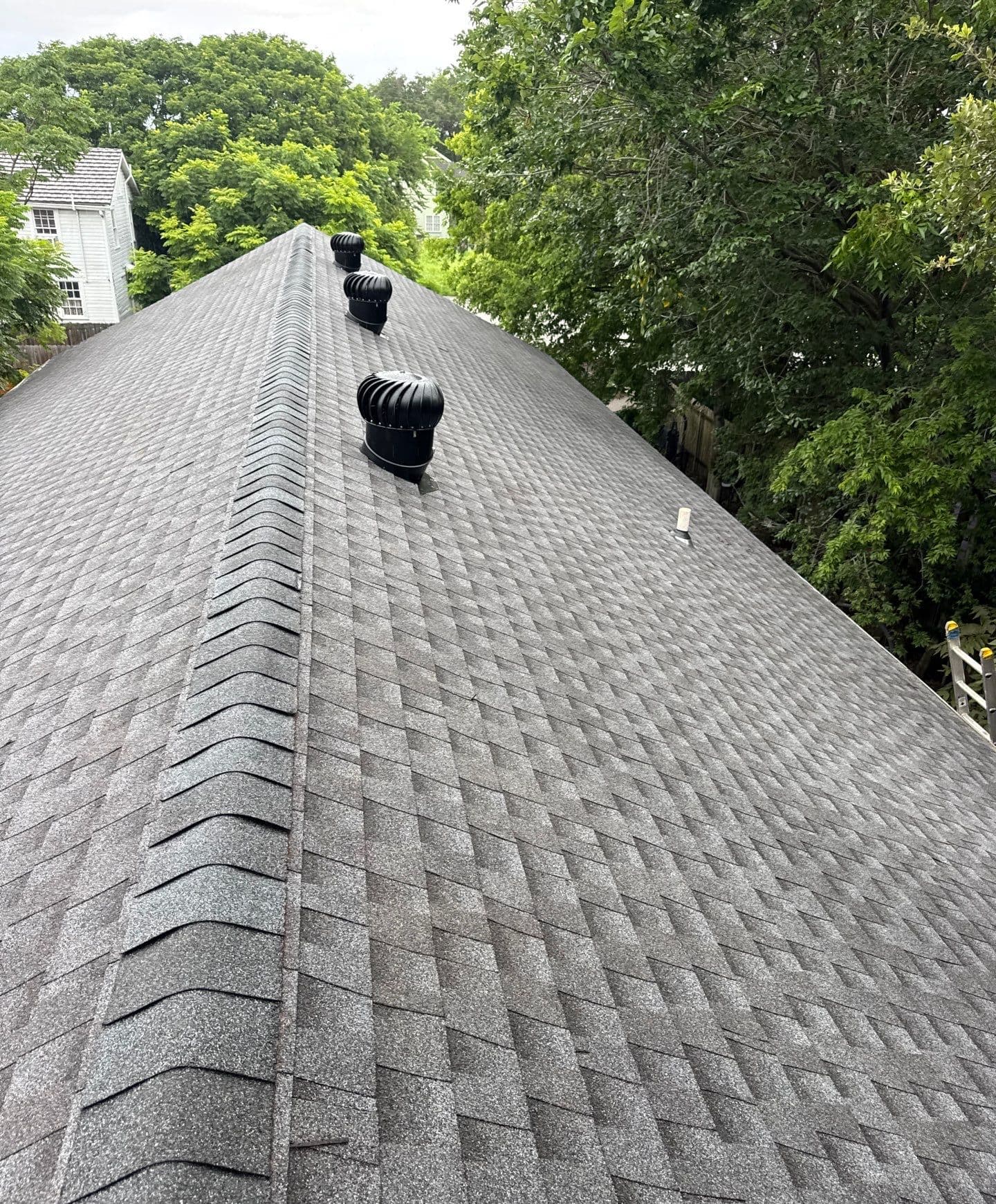Long capped shingle ridge beside three black turbine roof vents on a New Orleans replacement