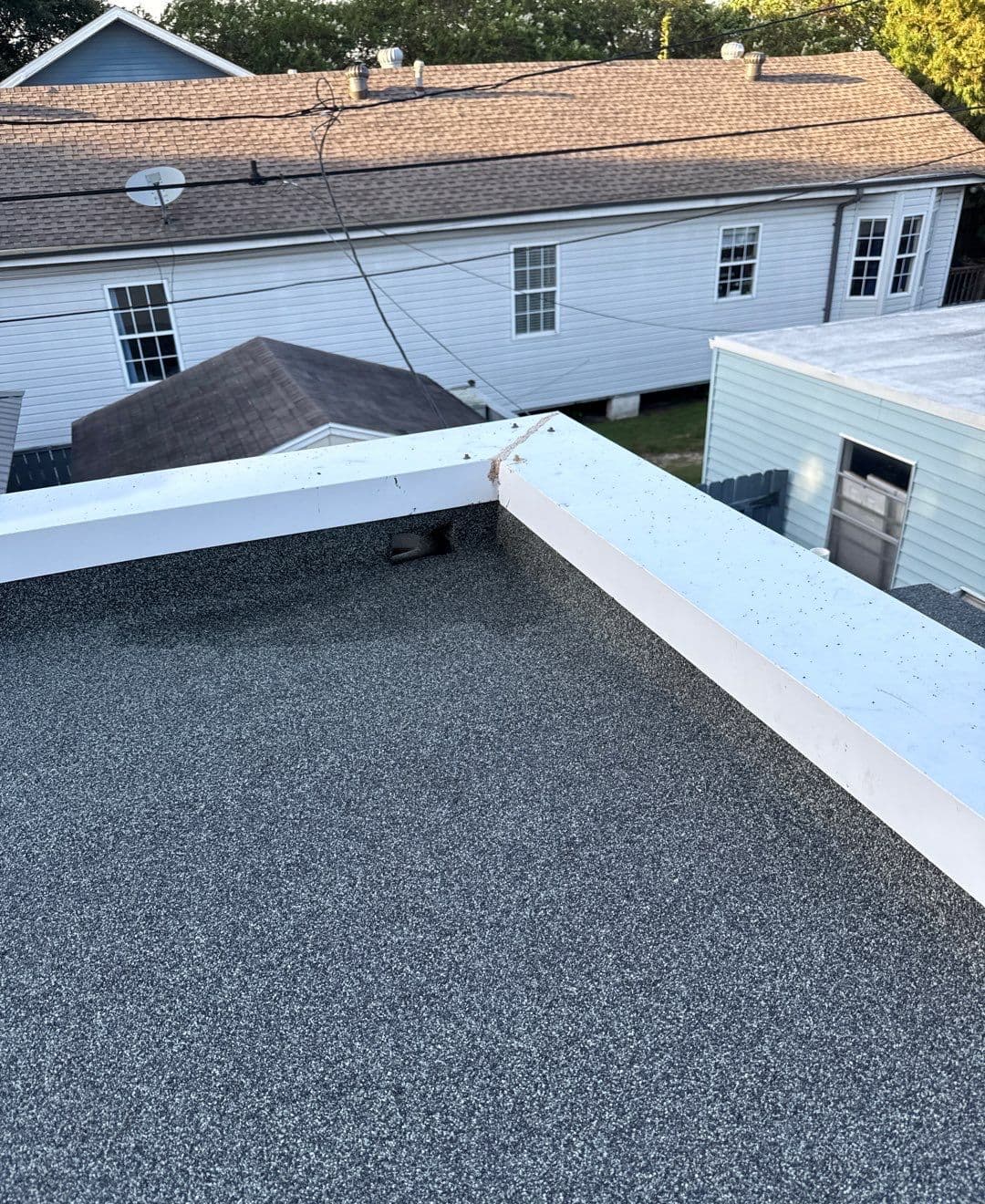 Granulated low-slope roof surface with white perimeter coping and a drainage opening on a New Orleans project
