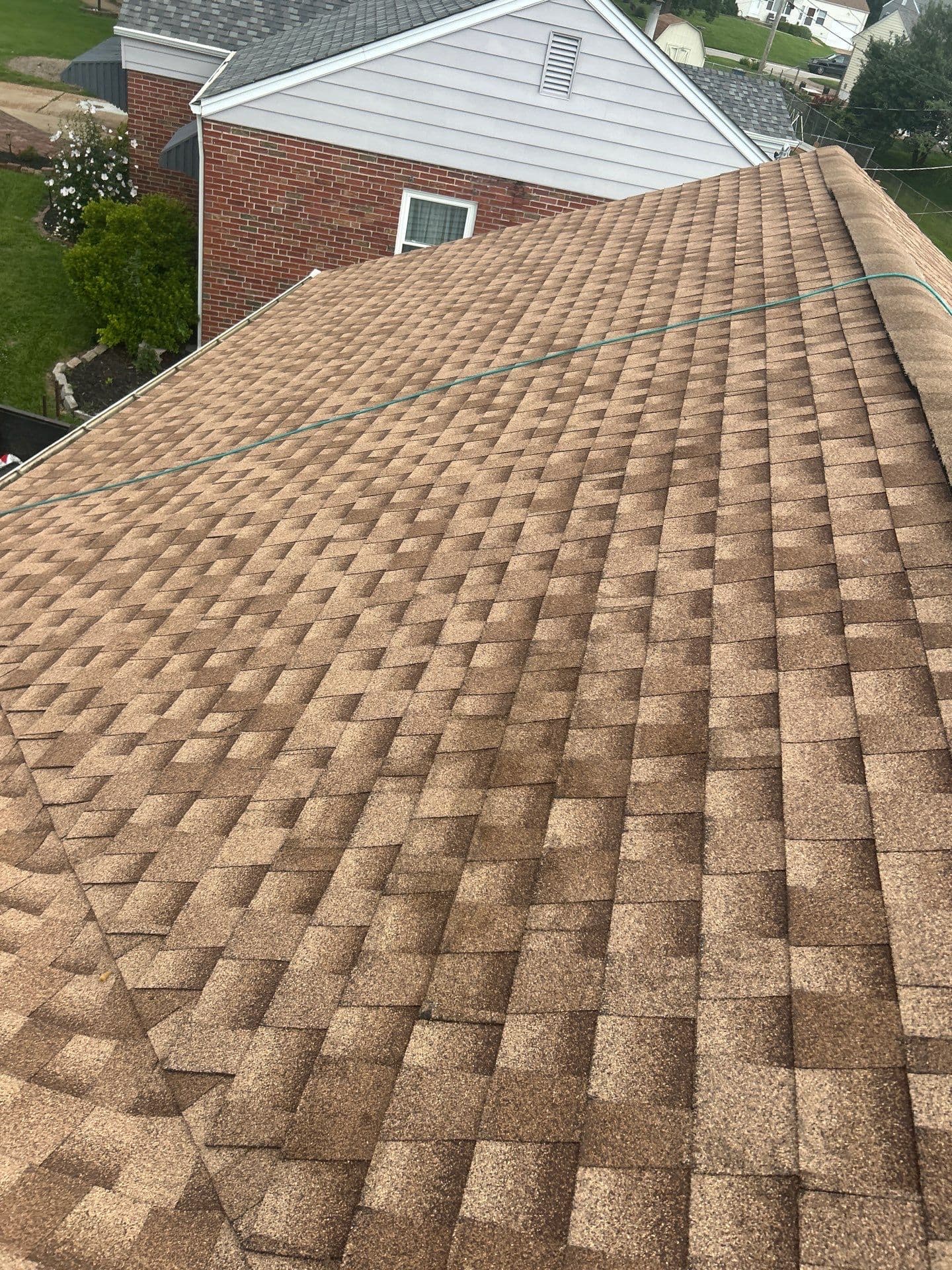 Brown architectural shingles and capped ridge during a St. Louis-area roof installation, with a hose still on the roof