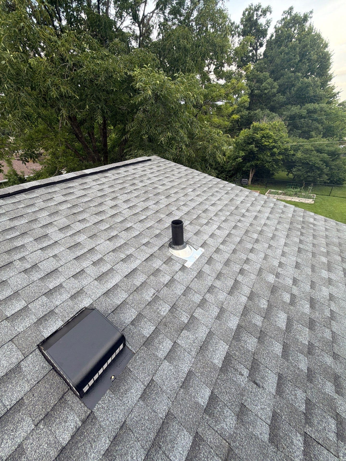 Gray shingles around a pipe penetration and box vent, with the ridge visible on a St. Louis-area roof