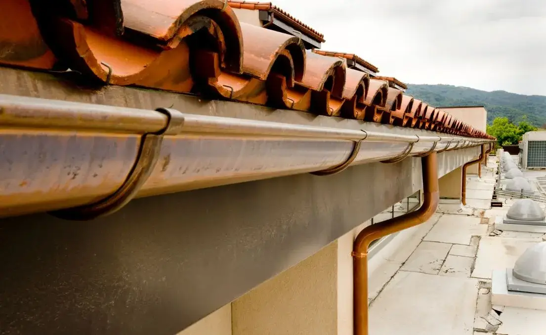 Finished copper gutter and downspout aligned beneath a clay tile roof edge