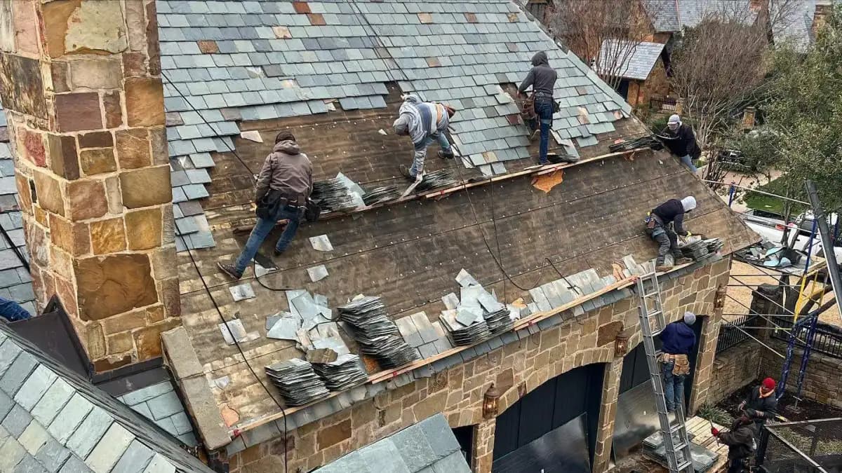 Roofing crew installing slate on a stone residence