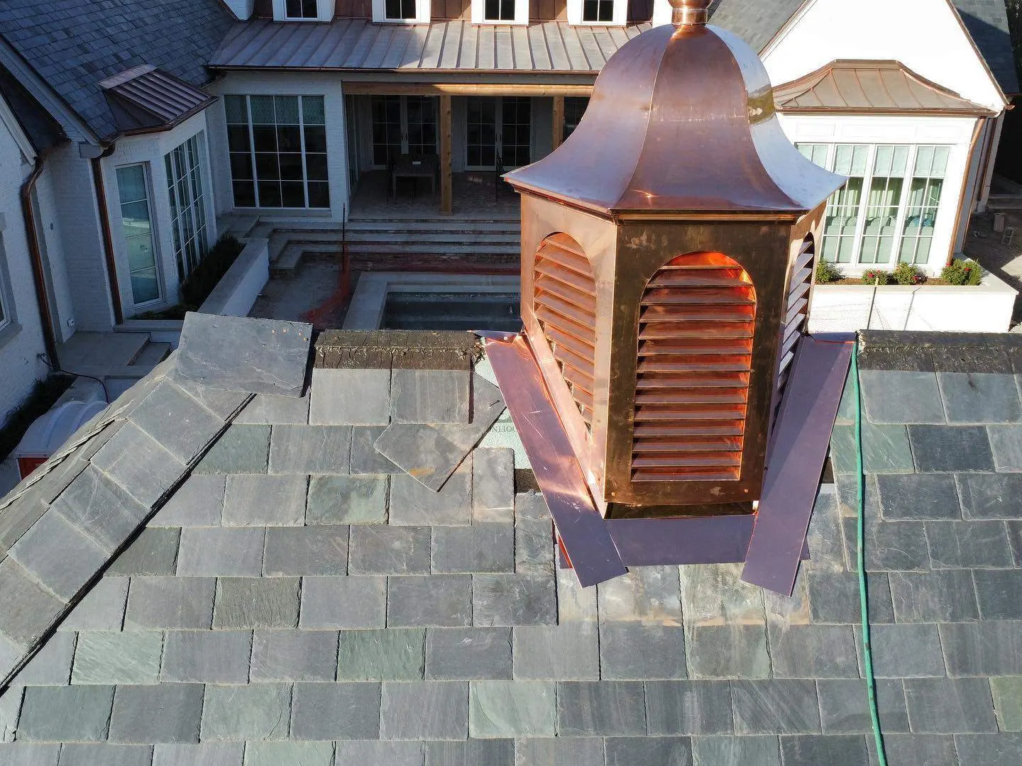 Copper cupola and standing-seam ridge on a finished slate roof, aerial detail